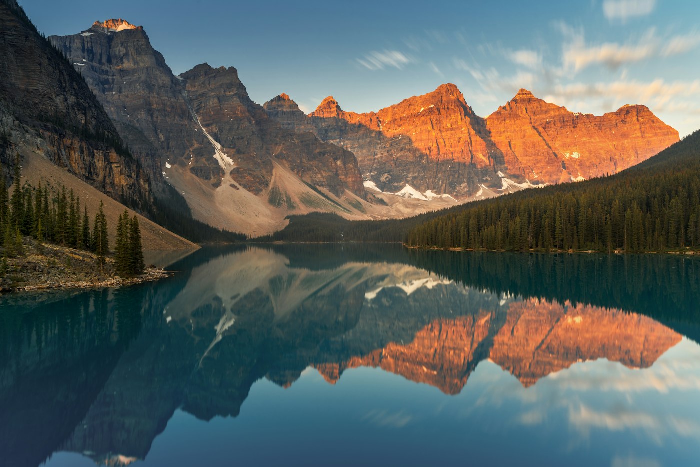 Sunrise lights the mountain peaks reflected in Moraine Lake